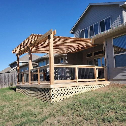 A newly built wooden deck with a pergola attached to a house in a suburban backyard.