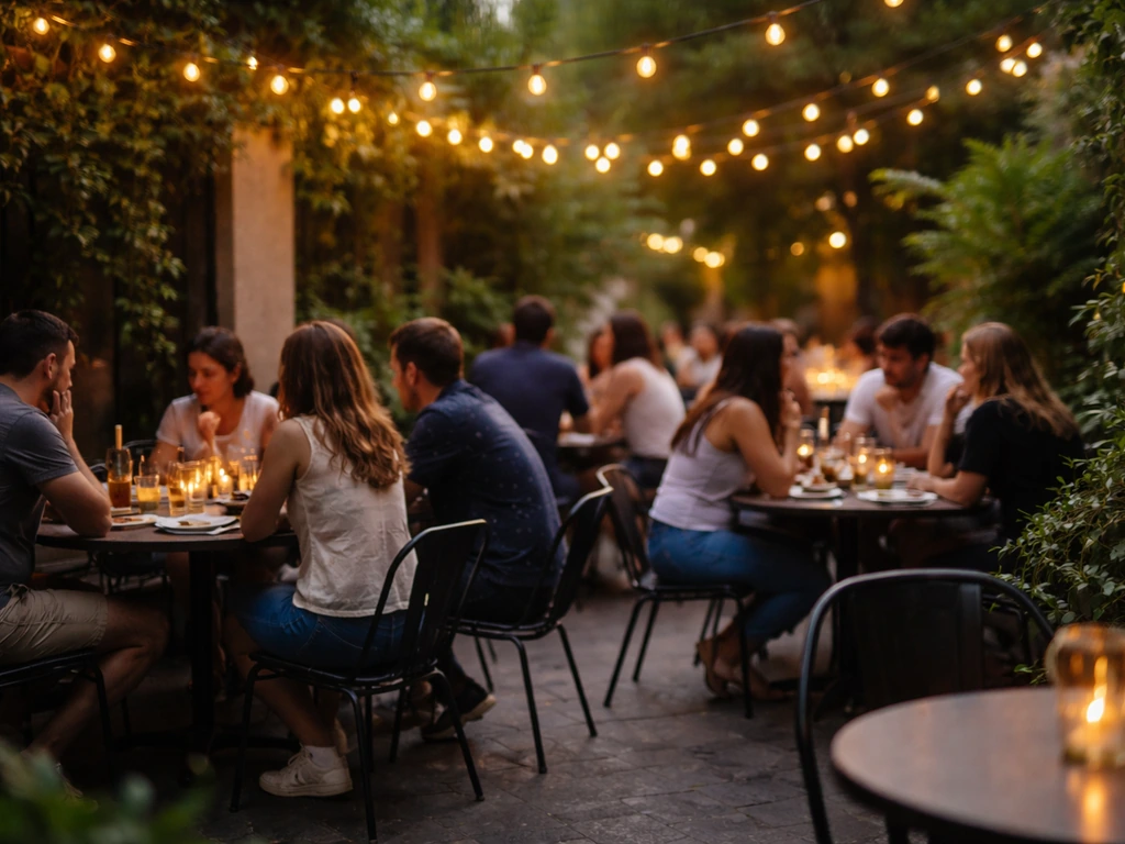 Warm early-evening patio with casual groups seated at small tables under soft string lights.