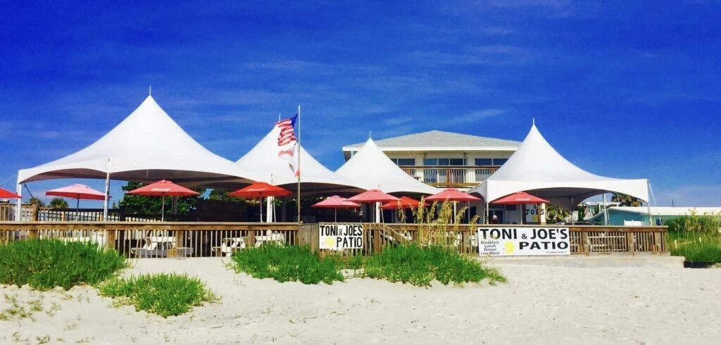 Toni & Joe’s Patio beachfront dining area with white canopy tents and umbrellas by the sand in New Smyrna Beach, Florida