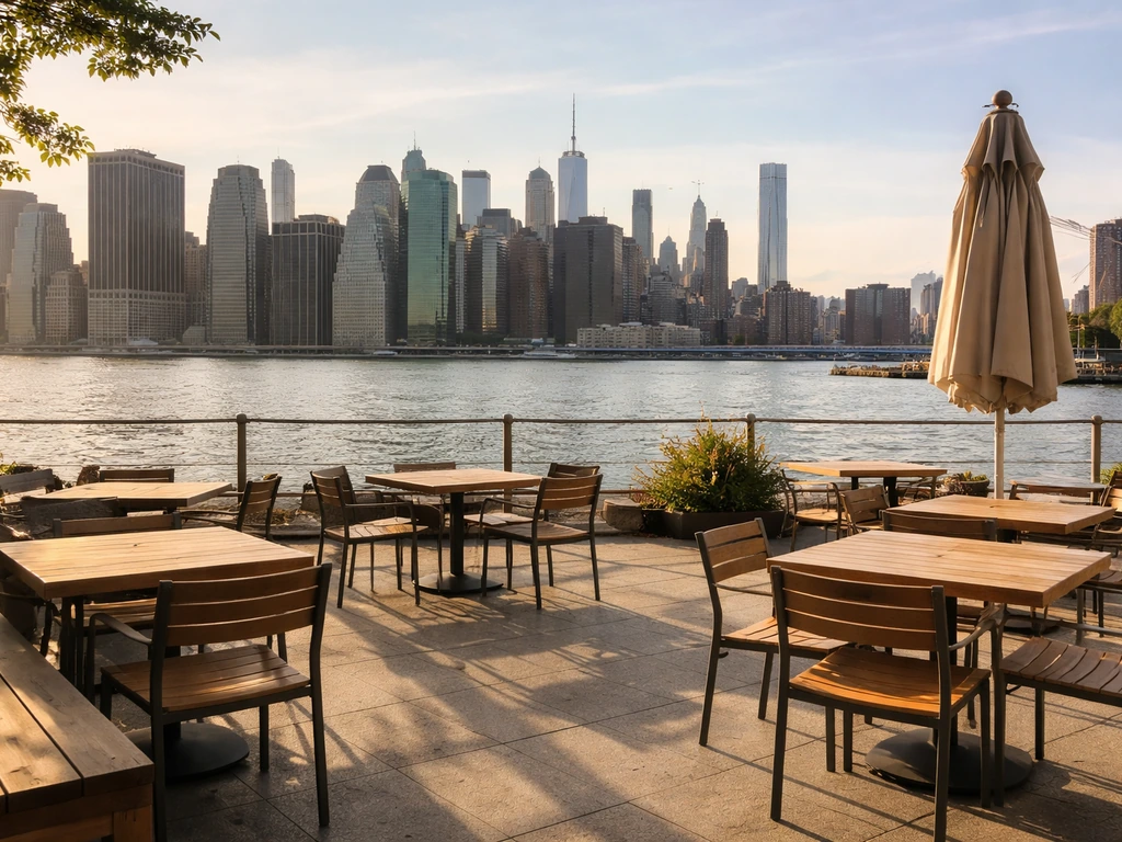 Open-air waterfront patio seating at Brooklyn Bridge Park with calm water and distant Manhattan skyline.