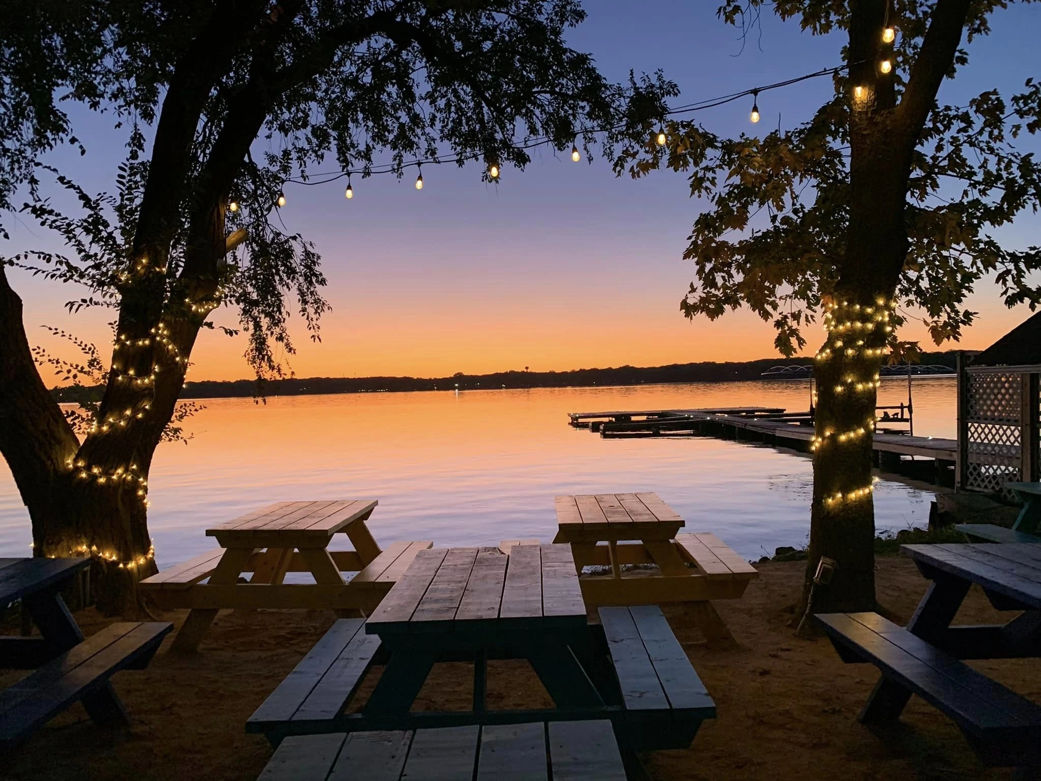 Outdoor patio seating by the water at sunset with string lights